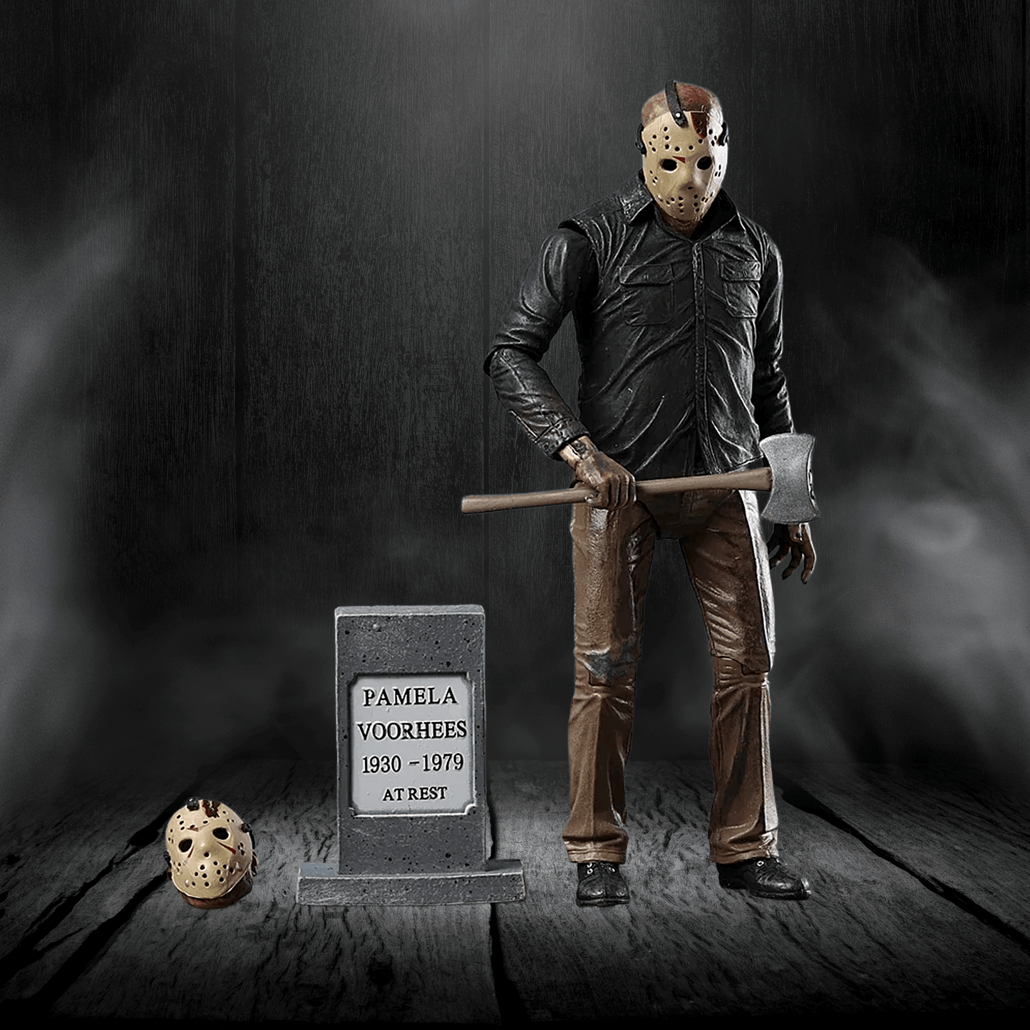 Action figure of a character holding an axe next to a tombstone with 'Pamela Voorhees' on it, against a dark background.