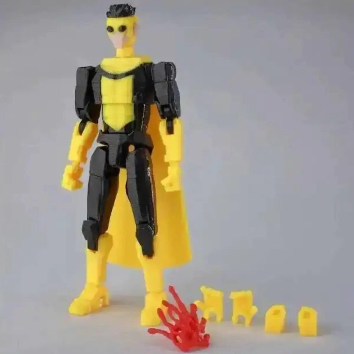 Toy figure with yellow and black suit, red hand, and small yellow figures on a gray background