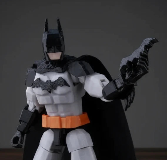 Toy figure of a superhero in a black and gray costume with a bat emblem, holding a weapon on a textured gray background.