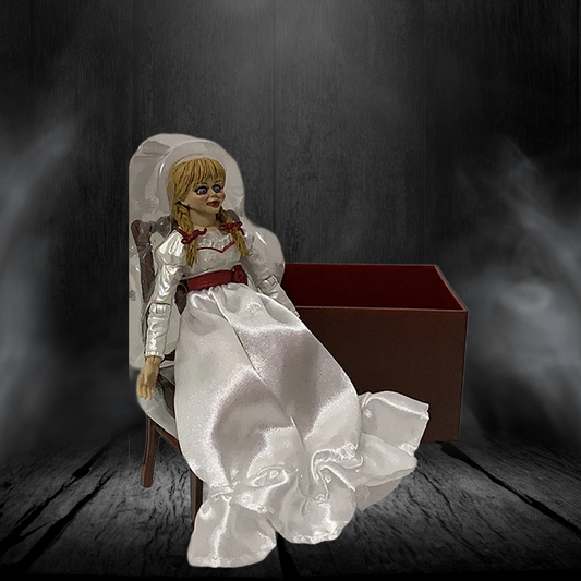 Horror doll in a white dress with red ribbon sitting on a chair against a dark background