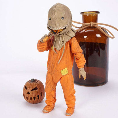 Scarecrow-like figure in an orange outfit with a hat, next to a carved pumpkin and amber glass bottle on a white background