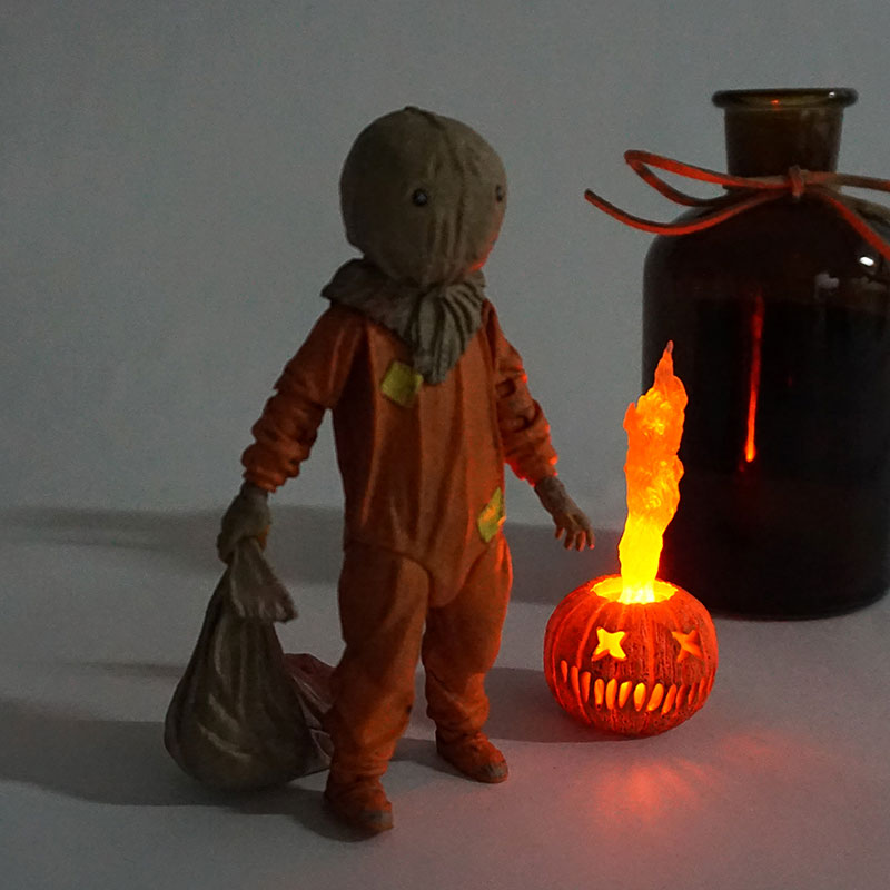Scarecrow figure with a lit jack-o'-lantern and dark bottle on a plain background