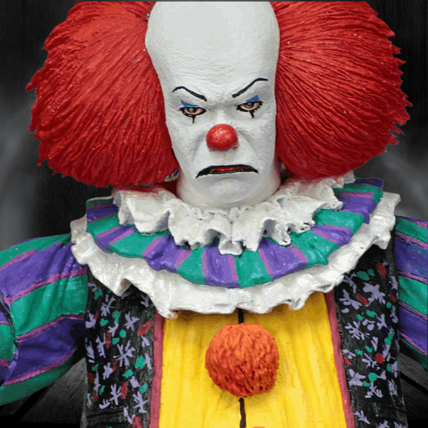 Clown with red hair and colorful outfit against a dark background