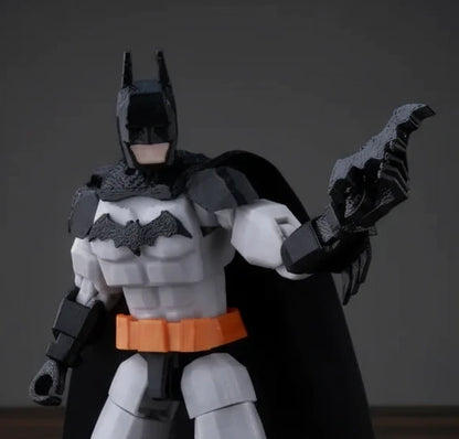 Toy figure of a superhero in a black and gray costume with a bat emblem, holding a weapon on a textured gray background.