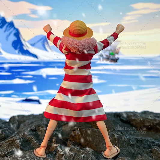 Figurine in a red and white striped outfit with a straw hat on a rocky surface with a mountain and water background.