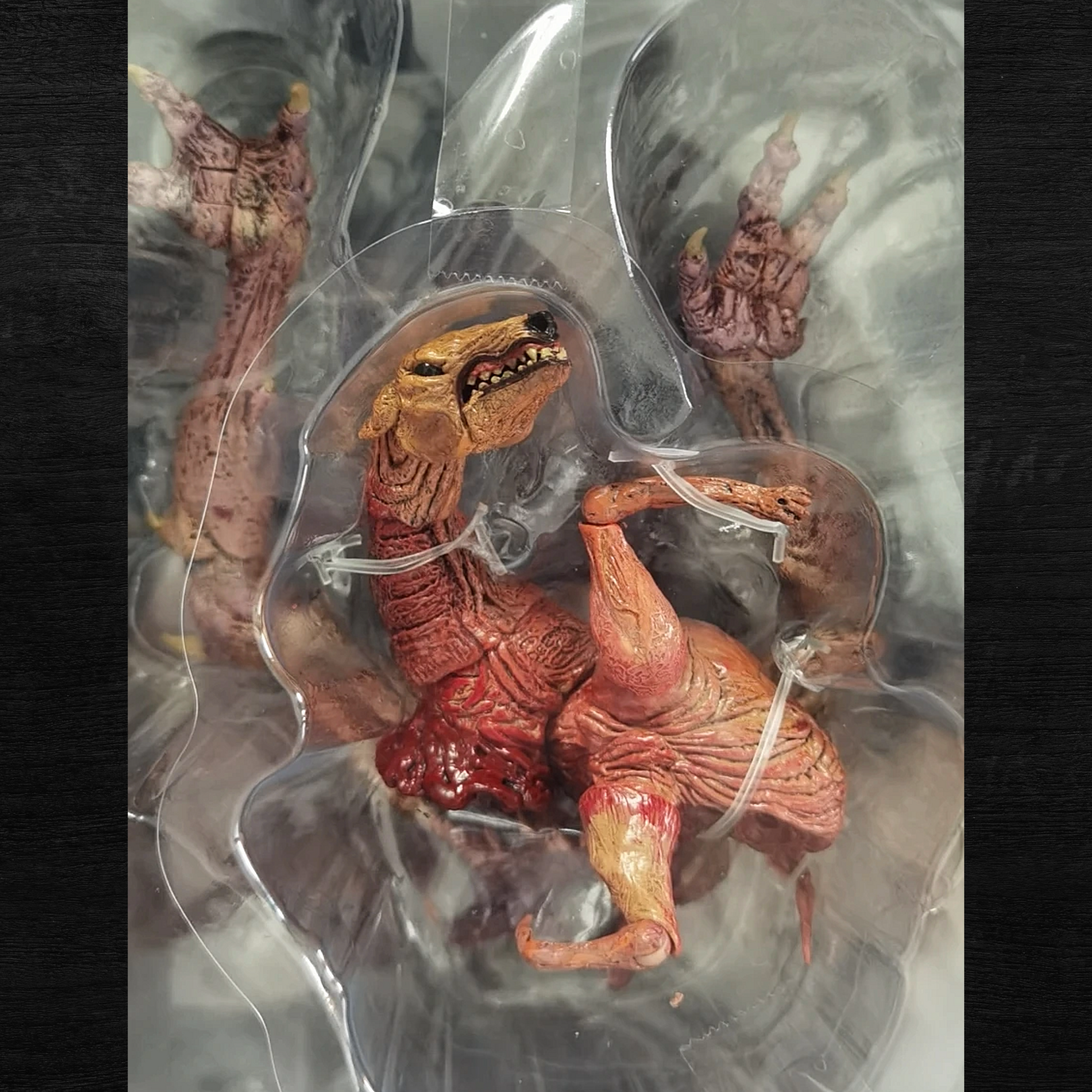 Toy figure of a red and brown creature in clear plastic packaging on a dark background